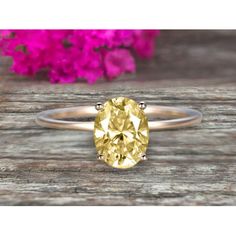 a yellow diamond ring sitting on top of a wooden table next to pink flower petals