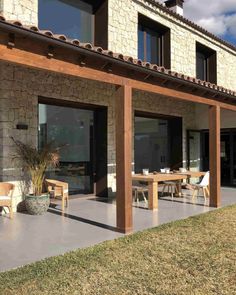 an outdoor dining area with wooden furniture and large windows on the side of a stone building