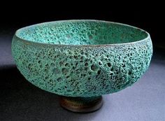 a green ceramic bowl sitting on top of a table next to a black wall and floor