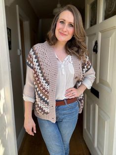 a woman standing in front of a door wearing jeans and a crocheted cardigan