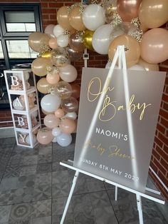 a baby shower sign and balloons in front of a brick wall at a baby's first birthday party