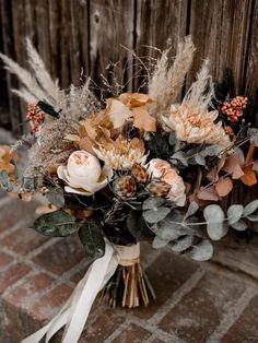 a bridal bouquet with feathers and flowers on a brick floor in front of a wooden fence