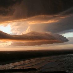 a large cloud hangs over the ocean at sunset