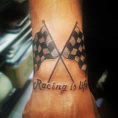 a wrist tattoo with two crossed checkered flags and the words racing is life on it