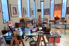 a glass table with many items on it in a room filled with chairs and pictures