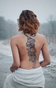 the back of a woman with a tiger tattoo on her upper body, wrapped in a towel