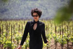 a woman wearing sunglasses and a black dress walking through a vineyard