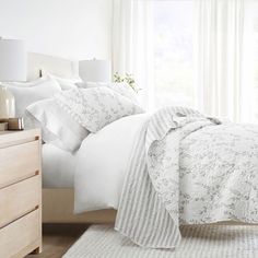 a bed with white comforter and pillows in a bedroom next to a window,