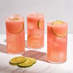 three glasses filled with watermelon and limeade on a marble counter top next to sliced lemons