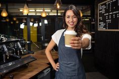 a woman standing in front of a bar holding a coffee cup and smiling at the camera