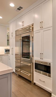 a stainless steel oven and microwave in a kitchen with white cabinetry, counter tops, and hardwood flooring