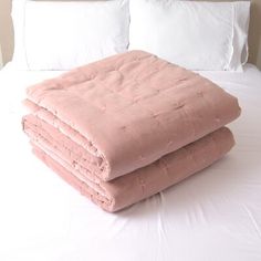 a bed with two blankets folded on top of it and pillows stacked up against the headboard