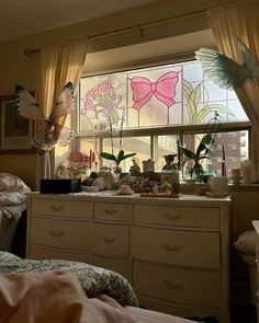 a bedroom with lots of clutter on the dressers and window sill in front of it