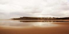 an empty beach with some water in the foreground and clouds in the sky above