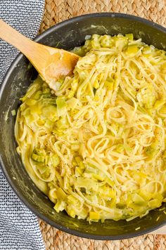 a pan filled with noodles and broccoli on top of a mat next to a wooden spoon