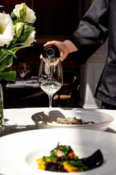 a person pouring wine into a glass on top of a white plate with flowers in the background