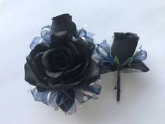 two black roses with blue and silver ribbons on top of each other next to a pen