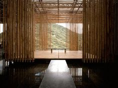 an open room with bamboo curtains and a bench in the center, surrounded by water