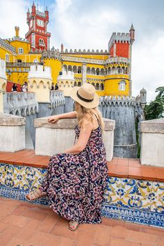 a woman in a hat is sitting on a wall looking at the castle behind her