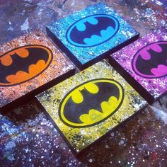 four painted batman coasters sitting on top of a table next to paint splatters