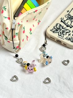 two charms are sitting on a table next to a cell phone and pen holder with pencils in it