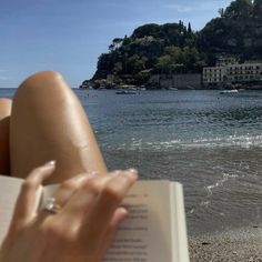 a woman is reading a book on the beach