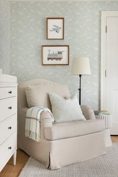 a living room with a chair, lamp and pictures hanging on the wall above it