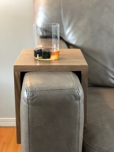 a small table with a glass on top of it next to a gray couch in a living room