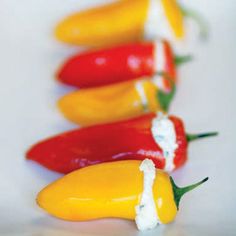 several peppers lined up in a row with white sauce on the top and one yellow pepper to the side