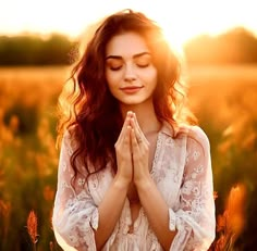 a woman standing in a field with her hands together and eyes closed to the sun