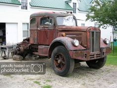 an old rusted out truck parked in front of a white house with a green roof