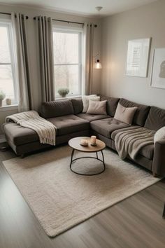 a living room with a sectional couch, coffee table and two windows in the corner