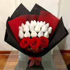 a bouquet of red and white roses in a black paper wrapper on top of a glass table