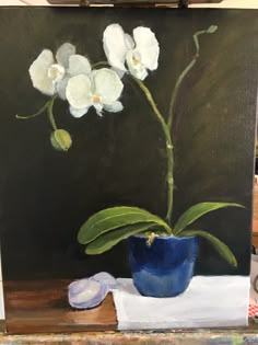 an oil painting of white flowers in a blue vase on a table next to a piece of paper