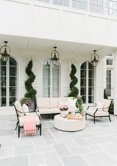 an outdoor living room with white furniture and potted plants on the side of the building