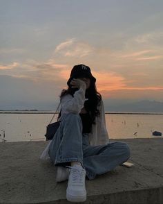 a woman sitting on the beach with her head in her hands while talking on a cell phone