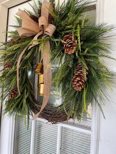 a wreath on the front door with pine cones and greenery