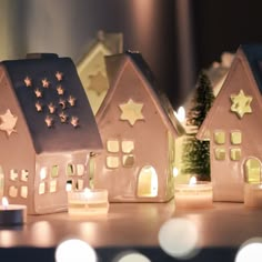 three small houses with lit candles in front of them on a table next to a christmas tree