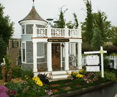 a small white house sitting in the middle of a garden with lots of flowers around it