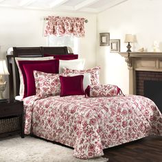 a bed with red and white comforter next to a fireplace