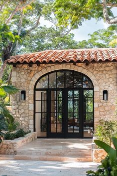 a stone house with an arched doorway and tiled roof, surrounded by lush greenery