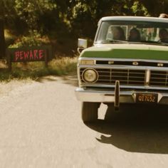 an old truck with people in the back driving down a dirt road next to trees