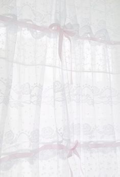 a white curtain with pink ribbon hanging from it's side