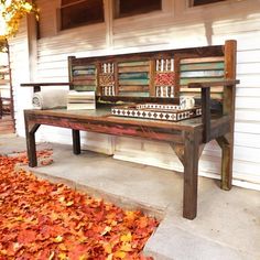 a wooden bench sitting in front of a white house with autumn leaves on the ground