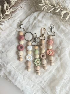 four key chains with flowers and beads hanging from them on a white cloth next to some dried grass