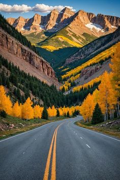 an empty road in the mountains with yellow trees on both sides and snow capped mountains behind it