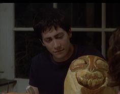 a man sitting at a table with a carved pumpkin in front of him and another person standing next to him