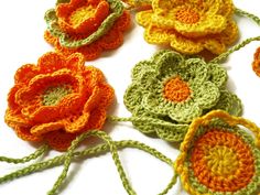 crocheted flowers are arranged on a white surface with green stems and orange centers