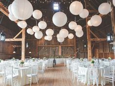 the inside of a barn with white tables and chairs, paper lanterns hanging from the ceiling