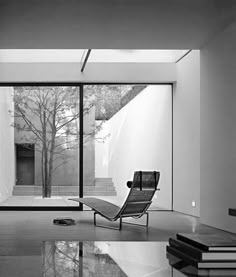 a black and white photo of a chair in front of a glass wall with stairs leading up to it